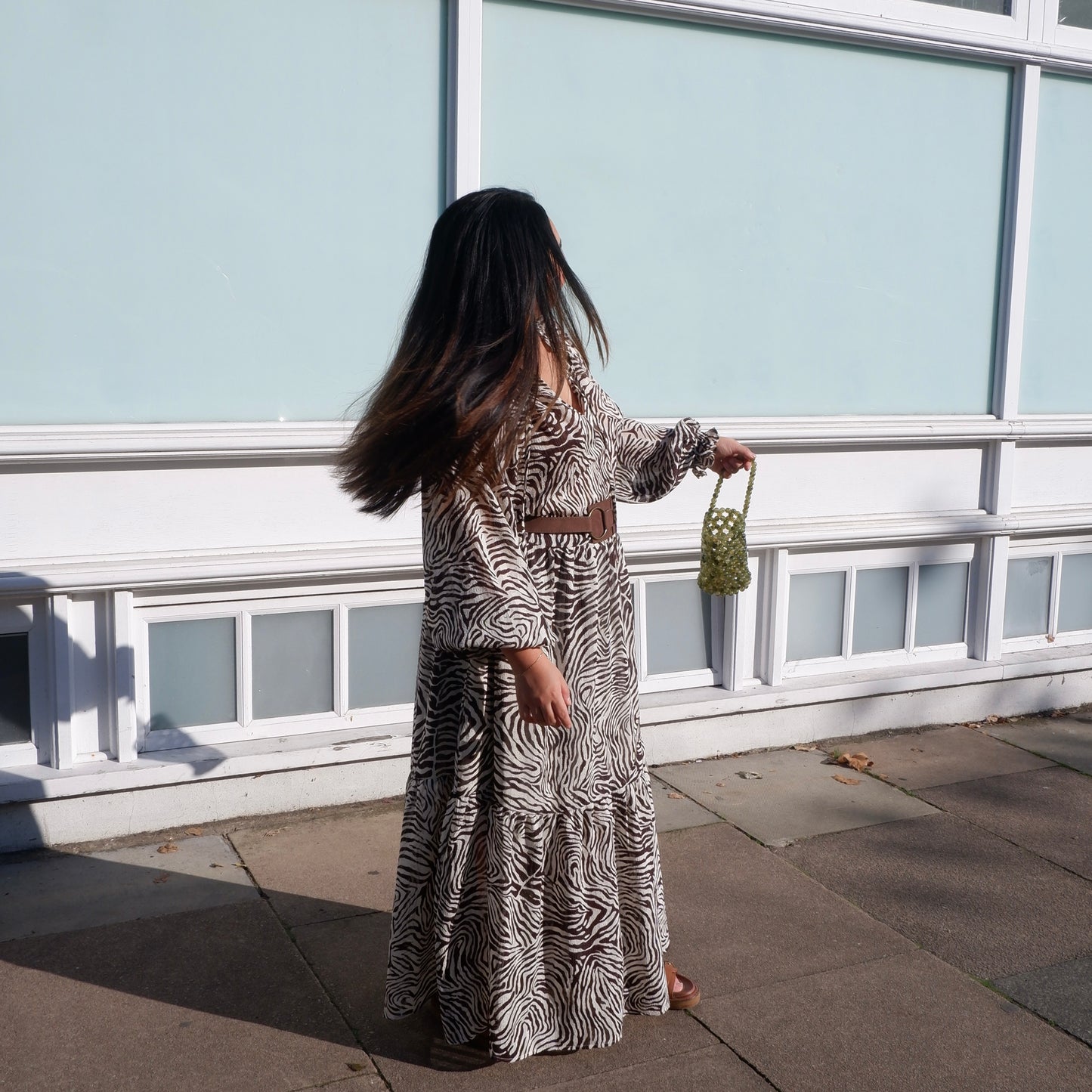 Person wearing a zebra print outfit standing on a sidewalk with a light blue building in the background.